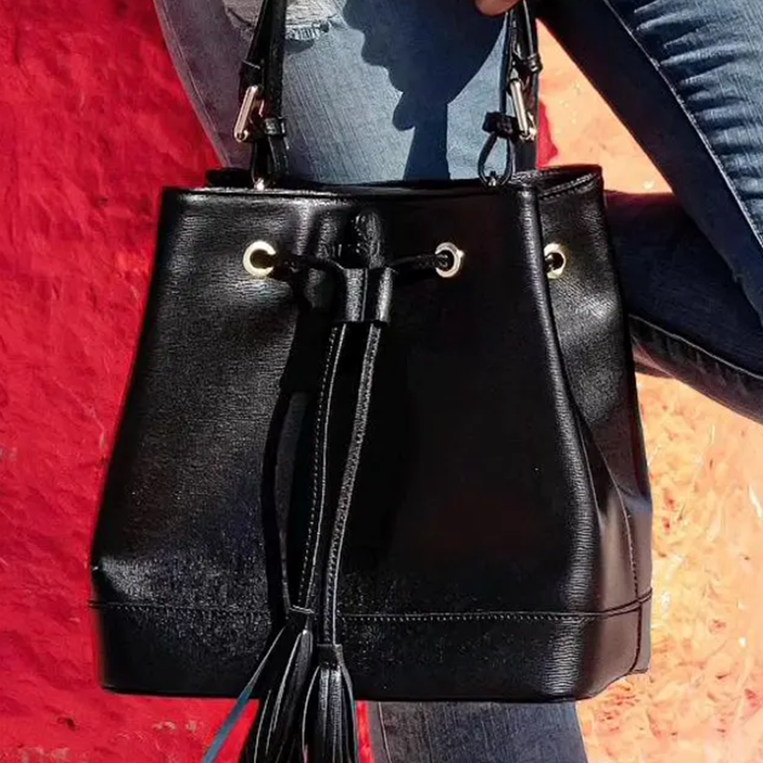 Glossy Jet Black Fine Grain Structured Bucket Handbag With Tassel Drawstring Cinch Rim, Integrated Short Top Loop And Perforated Adjustable Shoulder Strap Hardware